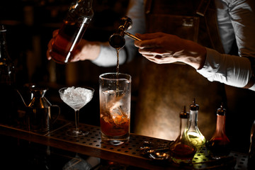 Male bartender pouring an alcohol from the steel jigger to the measuring glass cup