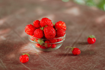 glass bowl full of strawberries on brown garden table  background