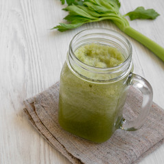 Green celery smoothie in a glass jar over white wooden background, low angle view. Copy space.