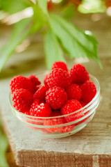 glass bowl full of raspberries on wooden garden table  background