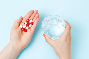 Female hand holding glass of water and pills, top view
