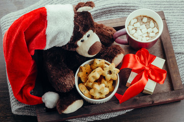 top view  wooden tray with teddy bear in Santa Claus ,gift box, warming beverage and gingerbread ,cozy winter holidays