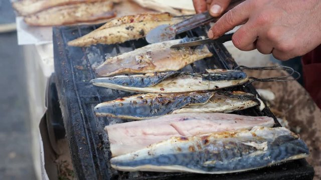 Traditional mediterranean cuisine. Man is grilling white fish balyk at street market, hands closeup. He turns fish and peel off scale. Local street food in Turkey.