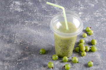 Fresh gooseberries smoothie in the plastic cup with drinking straw on the grey surface