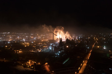 Aerial view of steel plant at night with smokestacks and fire blazing out of the pipe; industrial...
