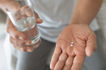 Man sitting on the bed while holding pills and a glass of water