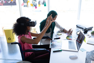 Female graphic designers using virtual reality headset and digital tablet at desk 