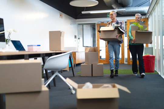 Male and female executives carrying cardboard boxes in office