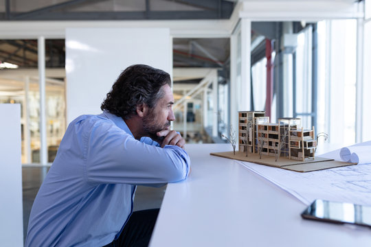 Male Architect Looking At Architectural Model At Table In A Modern Office