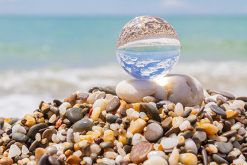 Obraz na płótnie Canvas Glass round ball on the beach reflects the sea in summer