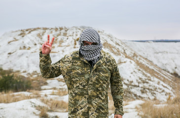 Naklejka premium Soldier is standing in the camouflage uniform and checkered bandana. Person is outdoors in the abandoned deserted place. Peaceful sign.