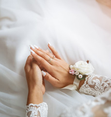 Obraz na płótnie Canvas Bride is holding hands on knees. Beautiful white manicure. Engagement rings on fingers. Wedding day details. Elegant accessories.