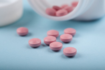 pink pills pouring out of the medicine bottle on blue background; medical treatment and safe use drug concept. closed up and selective focus 