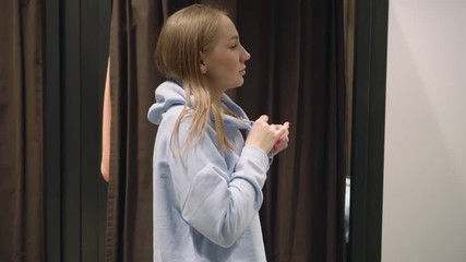 Pretty young woman trying on blue sweatshirt, puts a hood over her head