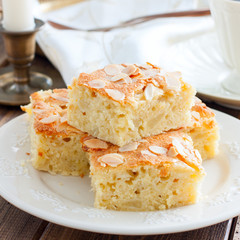 Sweet sliced apple pie with almond petals on a wooden table, square