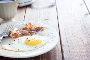 Traditional English breakfast of fried eggs with bacon on a wooden table, horizontal, place for text