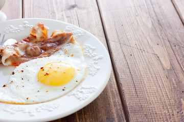 Traditional English breakfast of fried eggs with bacon on a wooden table, horizontal, place for text