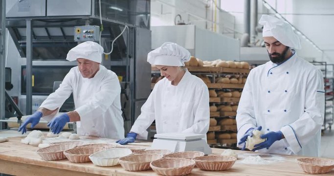 Professional bakers forming pieces of dough to baking bread on a big table in commercial kitchen industry