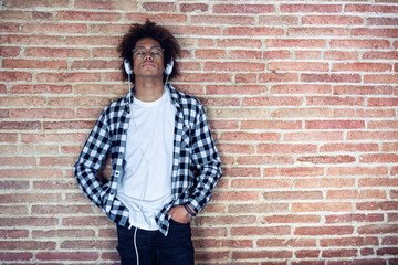 Relaxed afro-american young man listening to music with headphones leaning on stone wall at home.