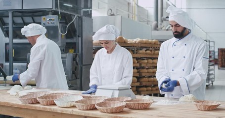 Three charismatic and stylish bakers woman and men working hard with dough making pieces to baking bread. slow motions