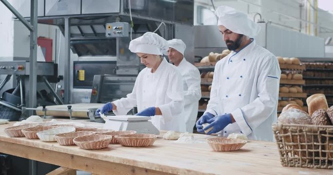 Baking industry three professional bakers working concentrated with dough they prepare for baking the bread , stylish dress code. shot on red epic