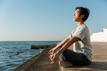 Fototapeta na wymiar Calm healthy asian man doing yoga exercises at the beach