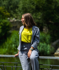 The woman in a gray stylish suit among greens sits in the park and has a rest. Portrait and emotions.