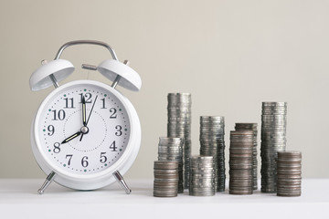 Alarm clock and coin piles arrange into growth chart on white background, finance and business concept