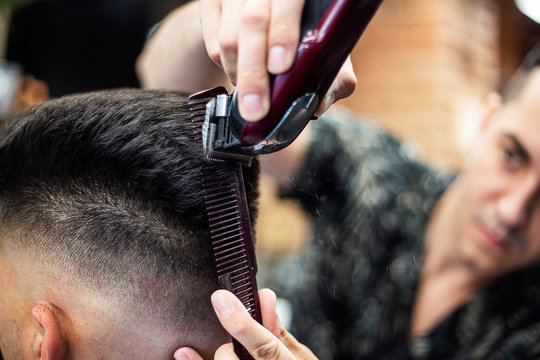 Rear view of young man getting a modern haircut. Man being trimmed with professional electric clipper machine in barbershop. Male beauty treatment concept. Guy getting new haircut in barber salon