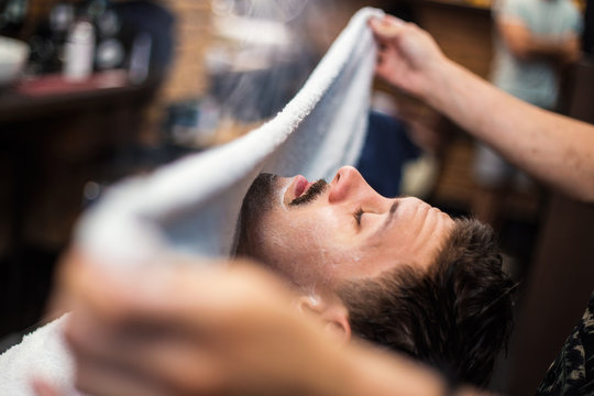 Barber covers the face of a man with a hot towel. Traditional ritual of shaving the beard with hot and cold compresses in a old style barber shop. Hot towel on face before shaving in barber shop