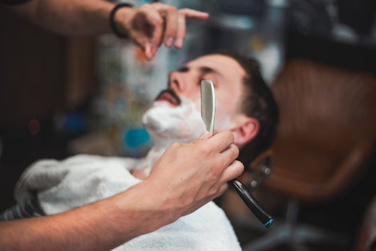 Man mith mustaches having a shave. Razor in hands of specialist barber. Young man getting an old-fashioned shave at the barber shop. Closeup, retro styled imagery