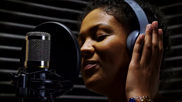 Female Vocalist Wearing Headphones Singing Into Microphone In Recording Studio