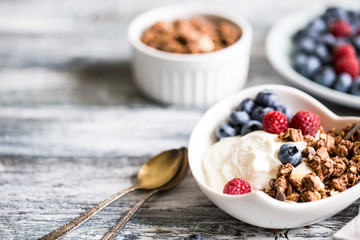 Greek yogurt, blueberries, raspberries and granola in a white bowl on a wooden background