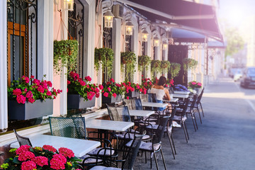 Summer restaurant on the city street. Outdoor cafe decorated with flowers. A young woman sitting at a table in a cafe in the sun.