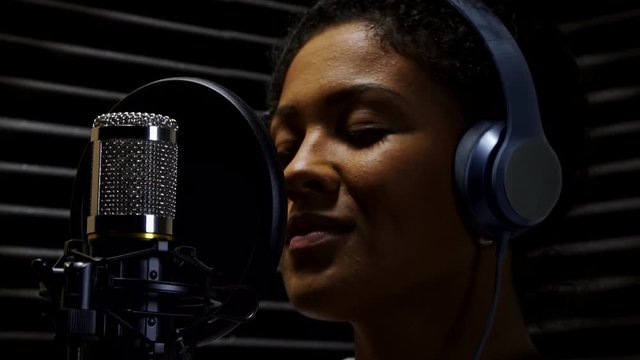 Female Vocalist Wearing Headphones Singing Into Microphone In Recording Studio