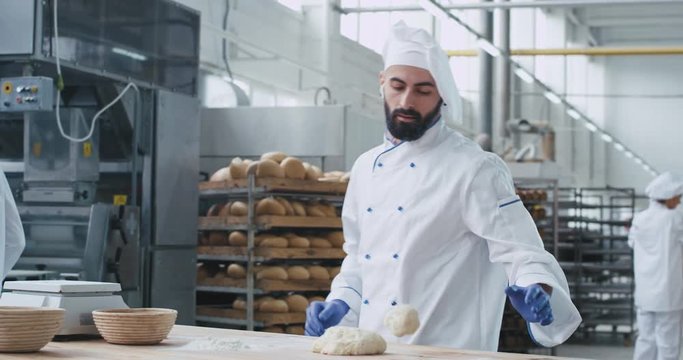 Two generations in a bakery industry old and young bakers enjoying the work together young man with wireless headphones dancing funny while preparing the dough old baker looking at him and smiling