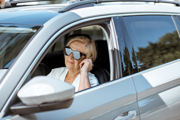 Beautiful senior business woman talking with phone while driving a modern car. Concept of an active people during retirement age