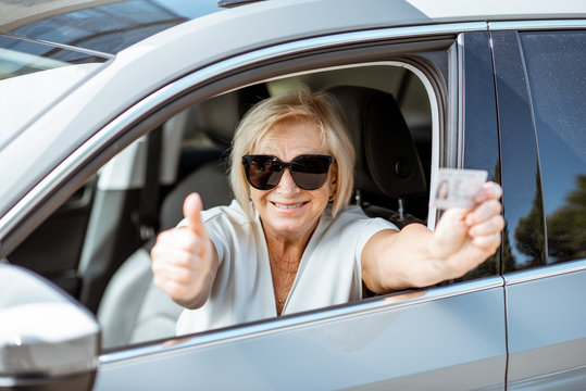 Portrait of a happy senior woman showing driver's license, while sitting in the car. Concept of an active people during retirement age