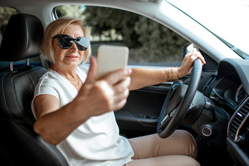 Senior business woman talking with smart phone while driving a car. Concept of an active people during retirement age
