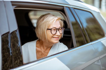 Portrait of a happy senior business woman looking out the car window, traveling on the back seat of...