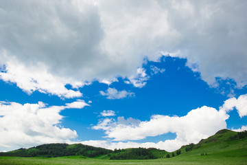 Fototapeta na wymiar Blue sky with white clouds, fields and meadows with green grass, on the background of mountains. Composition of nature. Rural summer landscape.