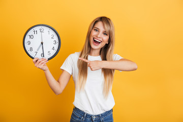 Cheery young blonde woman posing isolated over yellow wall background dressed in white casual...
