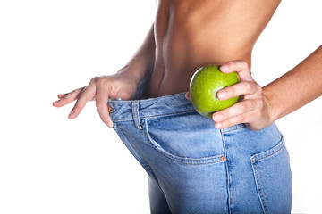 Young slim woman in blue jeans holding green apple, wearing oversize jeans. Isolated on white background. Diet concept