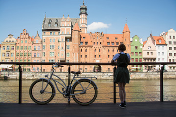 Young woman traveler with retro bicycle  stand near river in old gdansk city  - obrazy, fototapety, plakaty