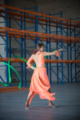 Young fit woman dancing with gymnastic ribbon in hands in the warehouse