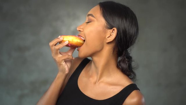 Portrait of beautiful young smiling woman in black t-shirt eating donut over concrete background