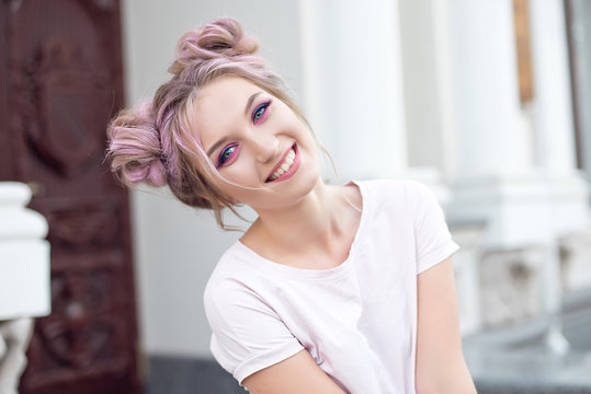 Happy cheerful young woman wearing her pink hair in a bun rejoicing at positive news or a birthday present, looking at the camera with a joyful and charming smile. Ginger student girl resting in the