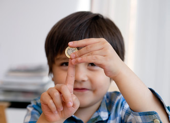 Blurry face of Kid holding one pound coin and showing one finger, Selective focus of happy child showing one pound for donation or saving money for future, little boy got one pound for donation.