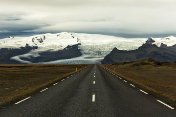 Deserted asphalt straight road on the background of glacial mountains. Landscapes of Iceland. The spirit of adventure and travel. The harsh nature of the north.