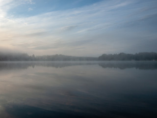 Fototapeta na wymiar Foggy and mystical lake landscape before sunrise. All silhouettes are blurry and unclear. Vaidavas lake, Latvia